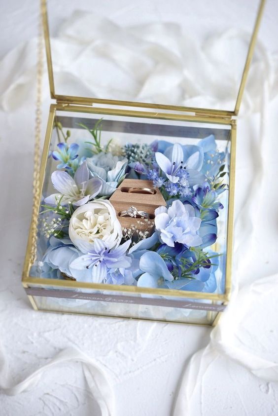 Wedding rings in a gold-framed glass box decorated with blue and white flowers